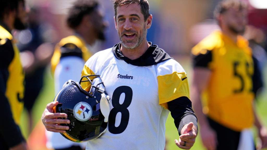 Pemain bintang NFL Aaron Rodgers mengenakan jersey latihan Pittsburgh Steelers sambil berbicara di hadapan para awak media olahraga.