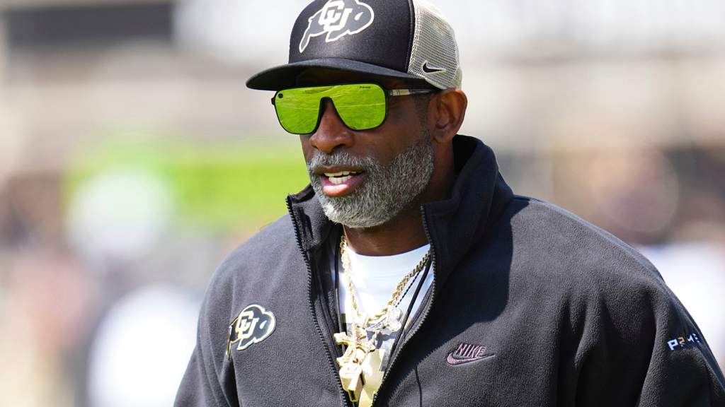 Pelatih sepak bola Amerika Deion Sanders memberikan arahan di pinggir lapangan sambil tersenyum.